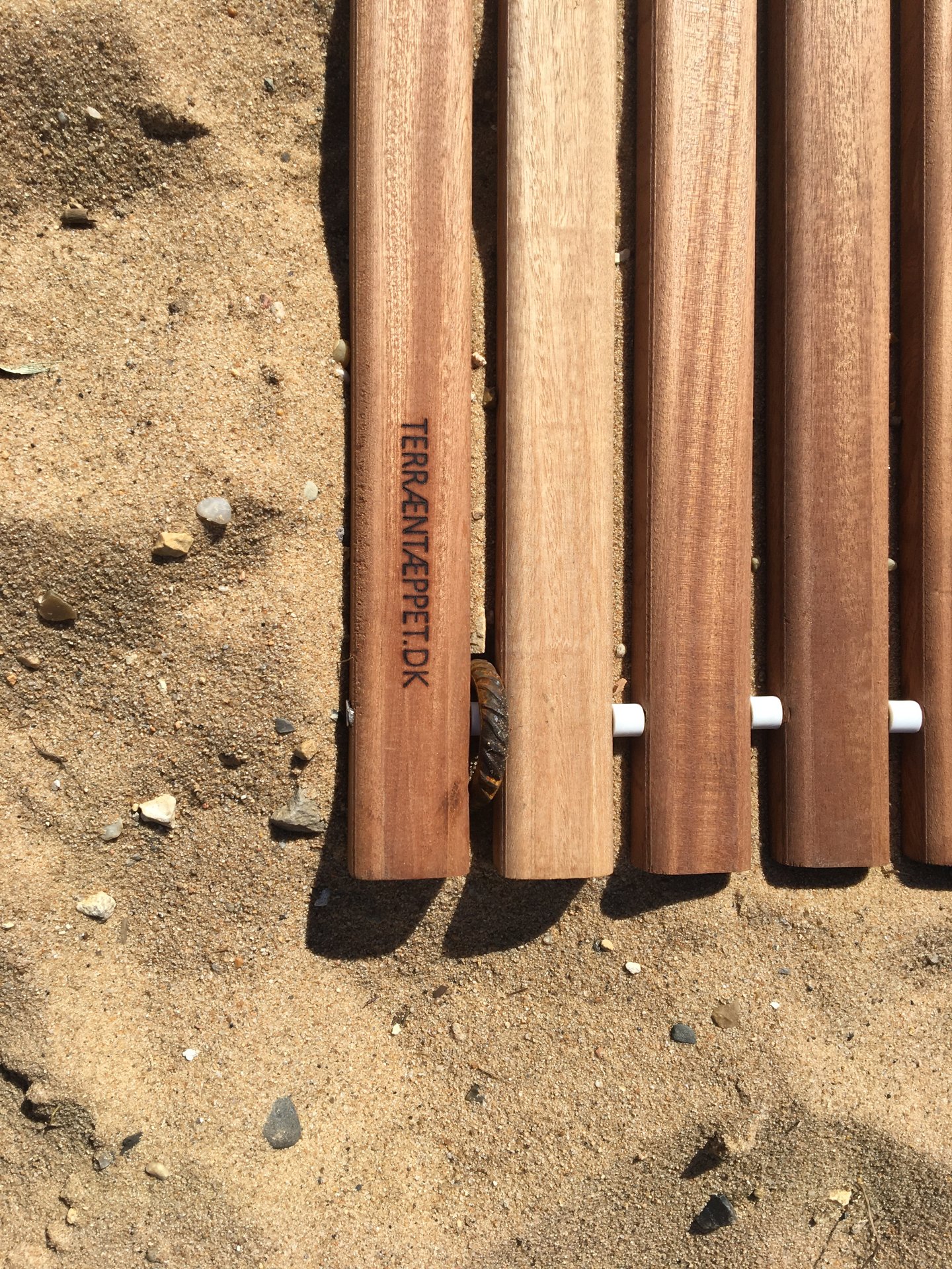 Detalje af terræntæppets mahogniplanker på sand